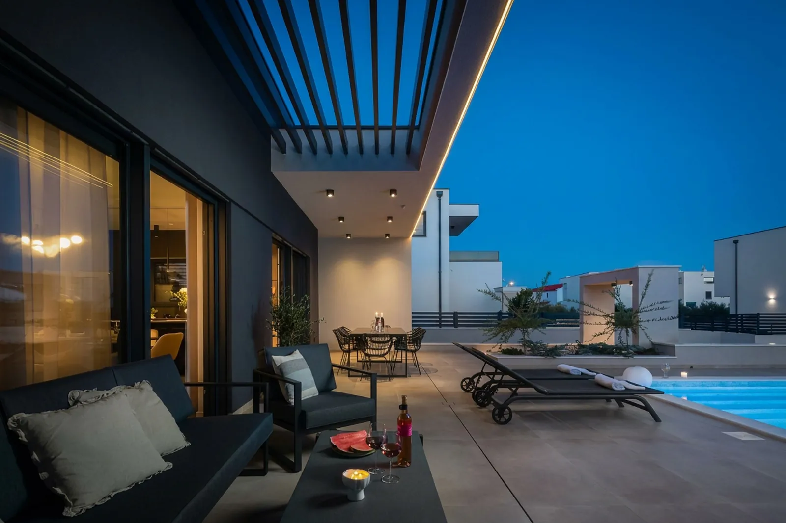 Covered terrace with lounger and pergola opening onto the pool at dusk