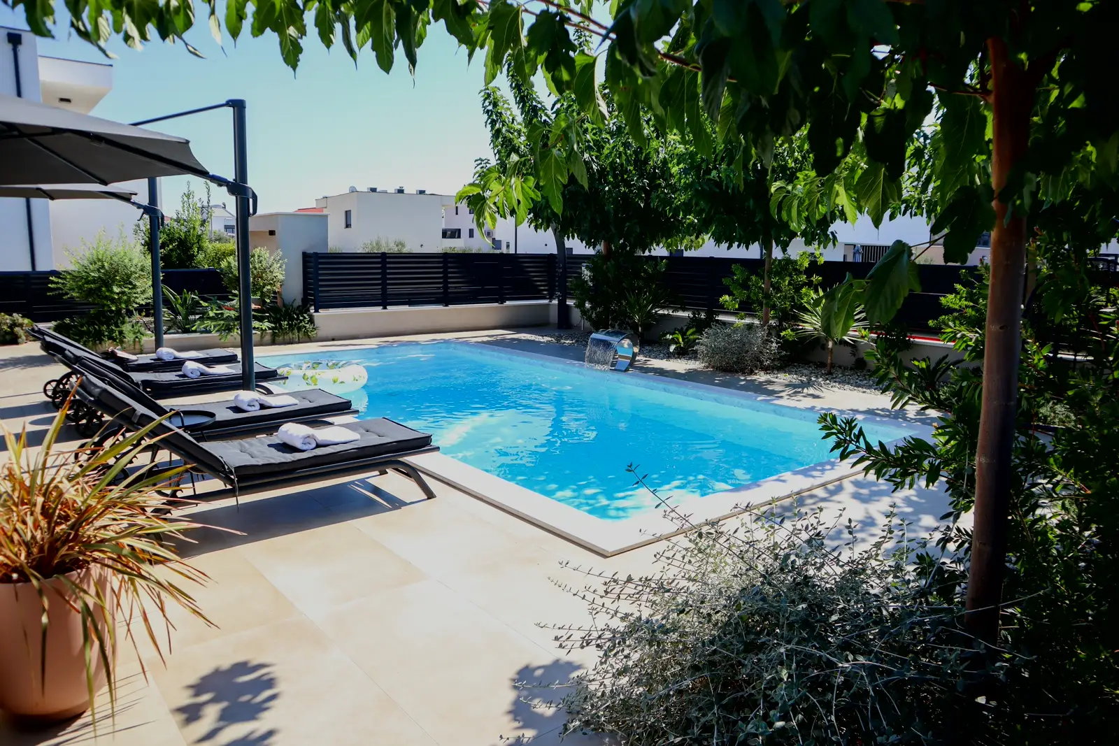 The pool seen from the house toward the surrounding trees, sun loungers to the left